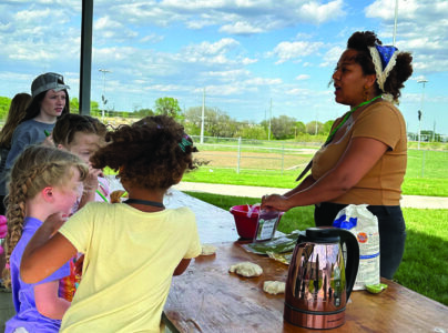 Outside under a pavilion, an adult teaches a hands-on activity f